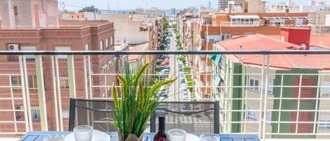 A balcony with a table set for dining, overlooking a cityscape with buildings and a clear sky.