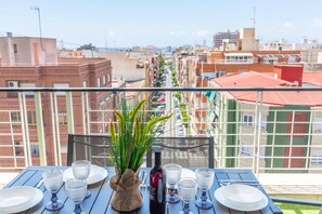 A balcony with a table set for dining, overlooking a cityscape with buildings and a clear sky. - Fidalsa Penthouse Amazing View (Alicante)