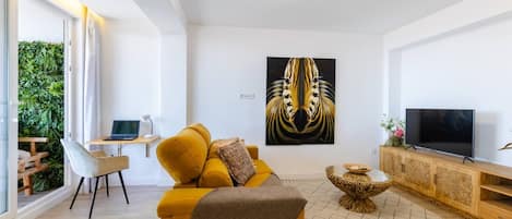 A modern living room with a sofa, a TV, a painting, and a desk with a laptop.