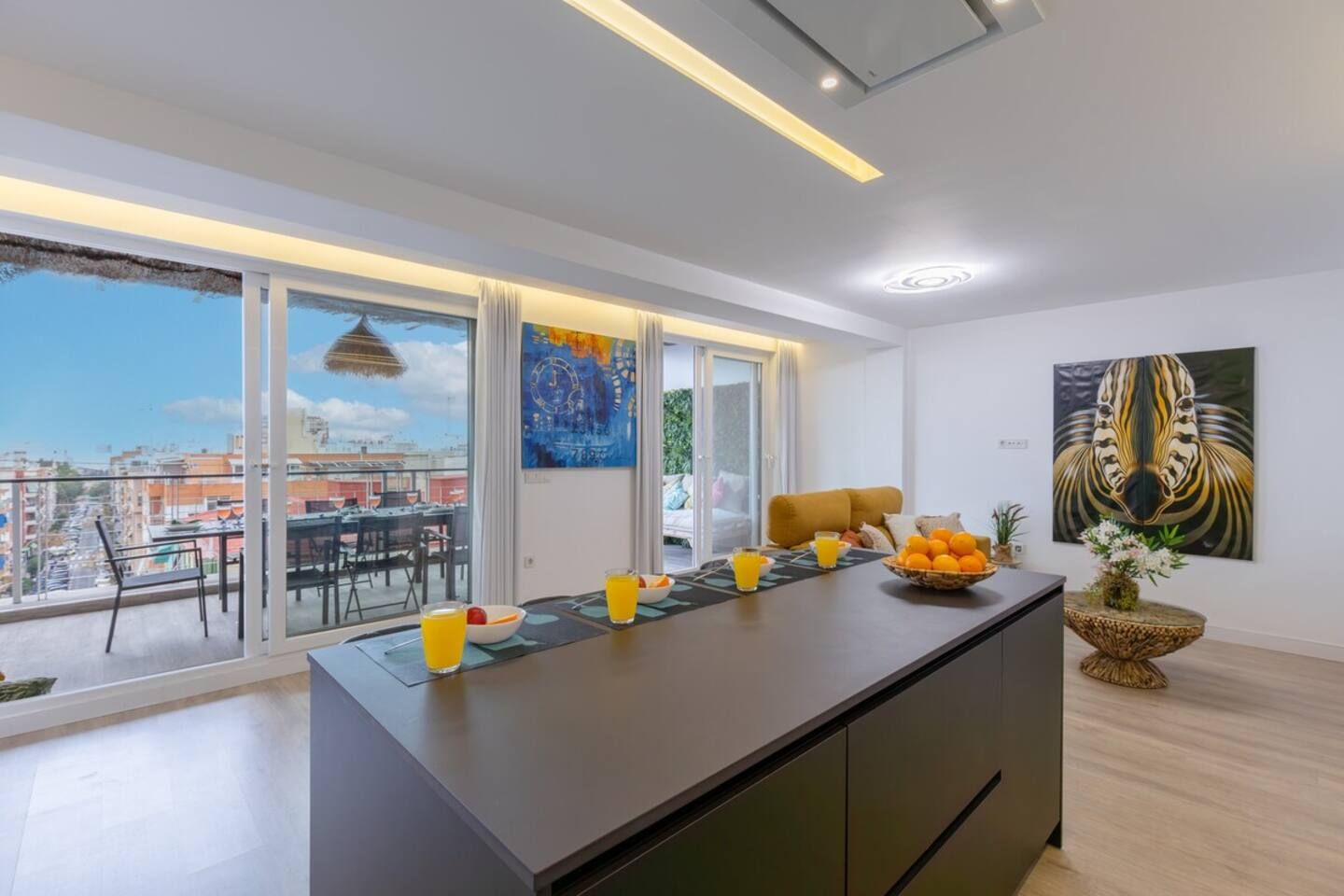 A modern kitchen with a large island, a dining area with a view, and a living space with artwork.