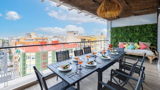 A balcony with a table set for dining, a hanging light fixture, and a green wall. - Fidalsa Penthouse Amazing View (Alicante)