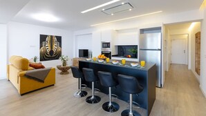 A modern kitchen with a central island, bar stools, a sofa, and a large abstract painting. - Fidalsa Penthouse Amazing View (Alicante)