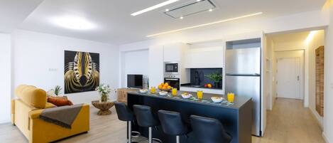 A modern kitchen with a central island, bar stools, a sofa, and a dining table.