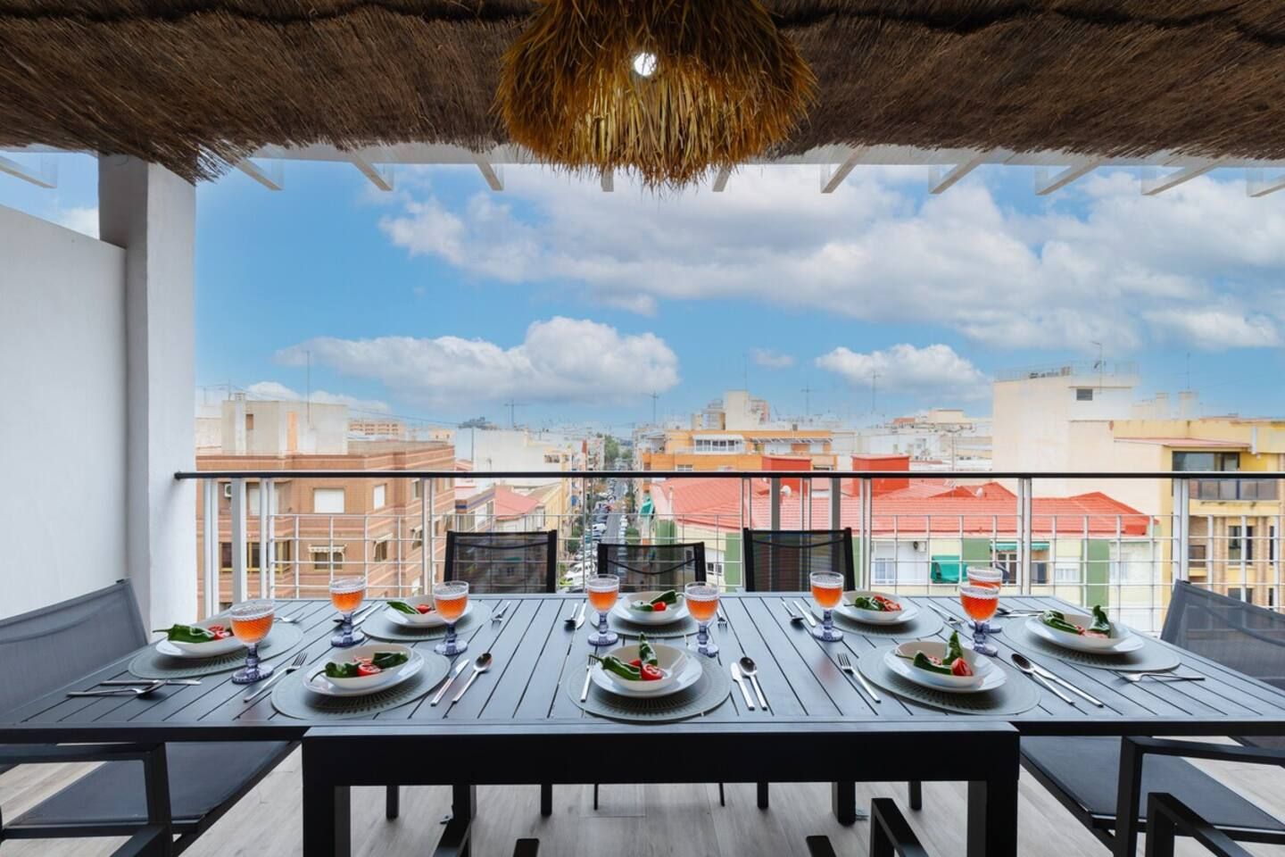 A dining table set for four with a city view, thatched ceiling, and a balcony railing.