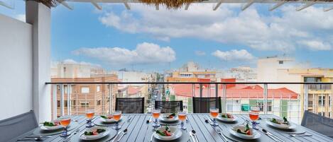 A dining table set for four with a city view, thatched ceiling, and a balcony railing.