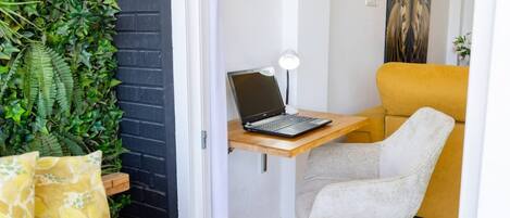 Ein Eckbüro mit einem Laptop auf einem Holztisch, einem Stuhl, einer Lampe und einer Wand mit Pflanzen.