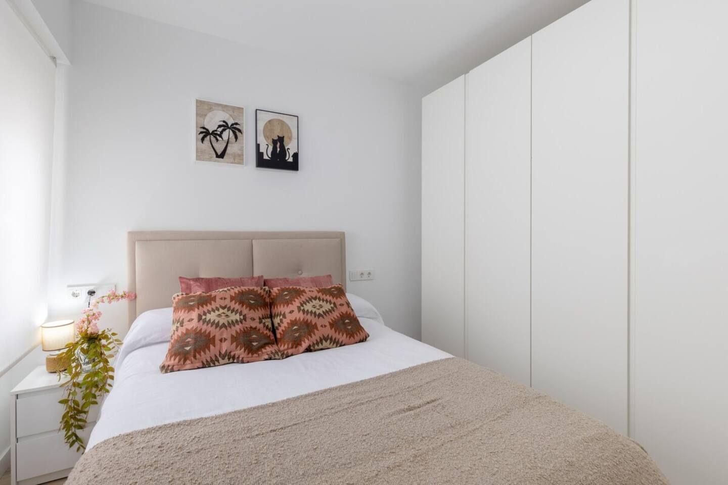 A bedroom with a bed, a nightstand, a lamp, a plant, and two wall art pieces.