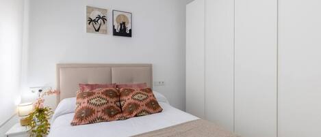 A bedroom with a bed, a nightstand, a lamp, a plant, and two wall art pieces.