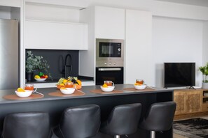 Eine moderne Küche mit Kochinsel, schwarzen Stühlen, einer Mikrowelle und einem Fernseher.