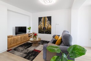 A modern living room with a flat-screen TV, a large abstract painting, a grey sofa, and a coffee table with a plant. - Fidalsa Penthouse Urban Sea View (Alicante)