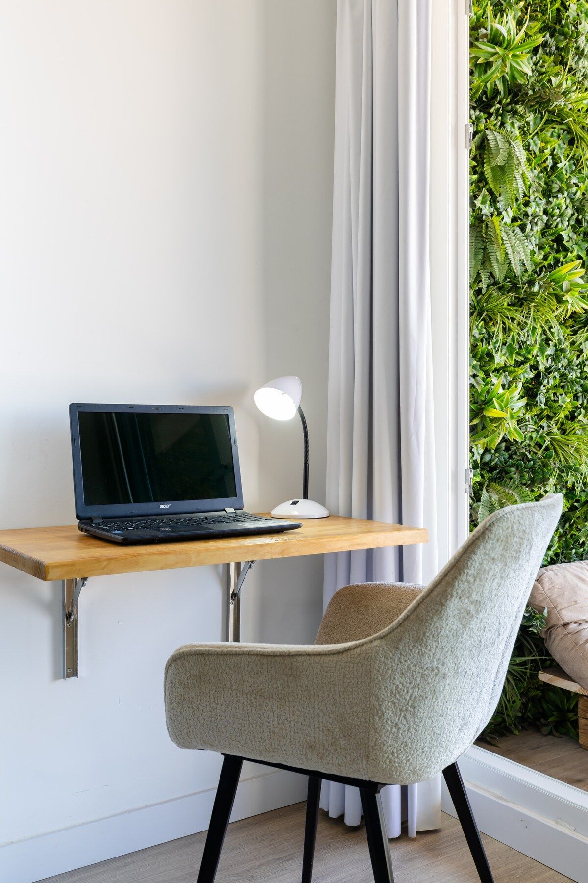 A laptop on a wooden desk, a white desk lamp, a chair, and a curtain.