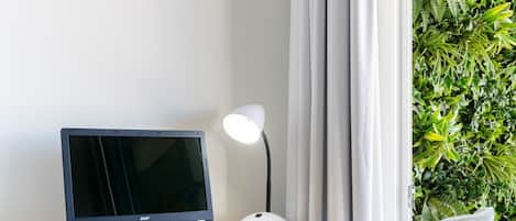 A laptop on a wooden desk, a white desk lamp, a chair, and a curtain.