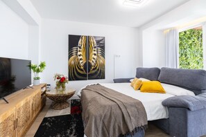 A modern bedroom with a bed, a grey sofa, a television, and a large abstract painting on the wall. - Fidalsa Penthouse Urban Sea View (Alicante)