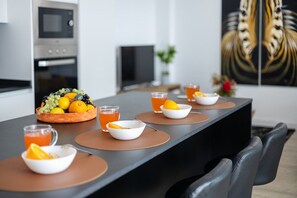 A modern kitchen with a dining table set for breakfast, featuring a fruit bowl, glasses of orange juice, and a bowl of cereal. - Fidalsa Penthouse Urban Sea View (Alicante)