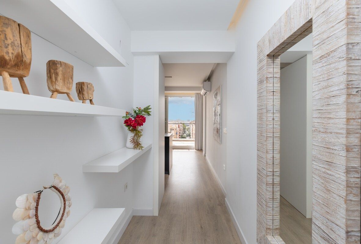 A narrow hallway with white walls, wooden flooring, and a view to the outside.