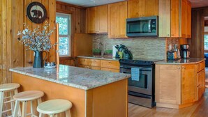 A kitchen with wooden cabinets, a granite countertop, a microwave, a stove, and bar stools.