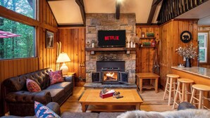 A cozy living room with a stone fireplace, leather sofa, and a Netflix sign above the TV.