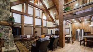 A spacious living area with a stone fireplace, leather sofas, and a high ceiling with exposed beams.
