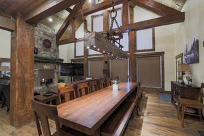 A spacious dining area with a long wooden table, stone wall, and exposed wooden beams.