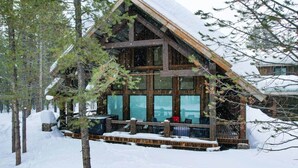 A log cabin with a porch, surrounded by snow and trees.