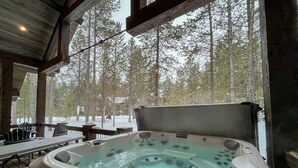 A hot tub in a covered outdoor area with a view of trees and a wooden deck.
