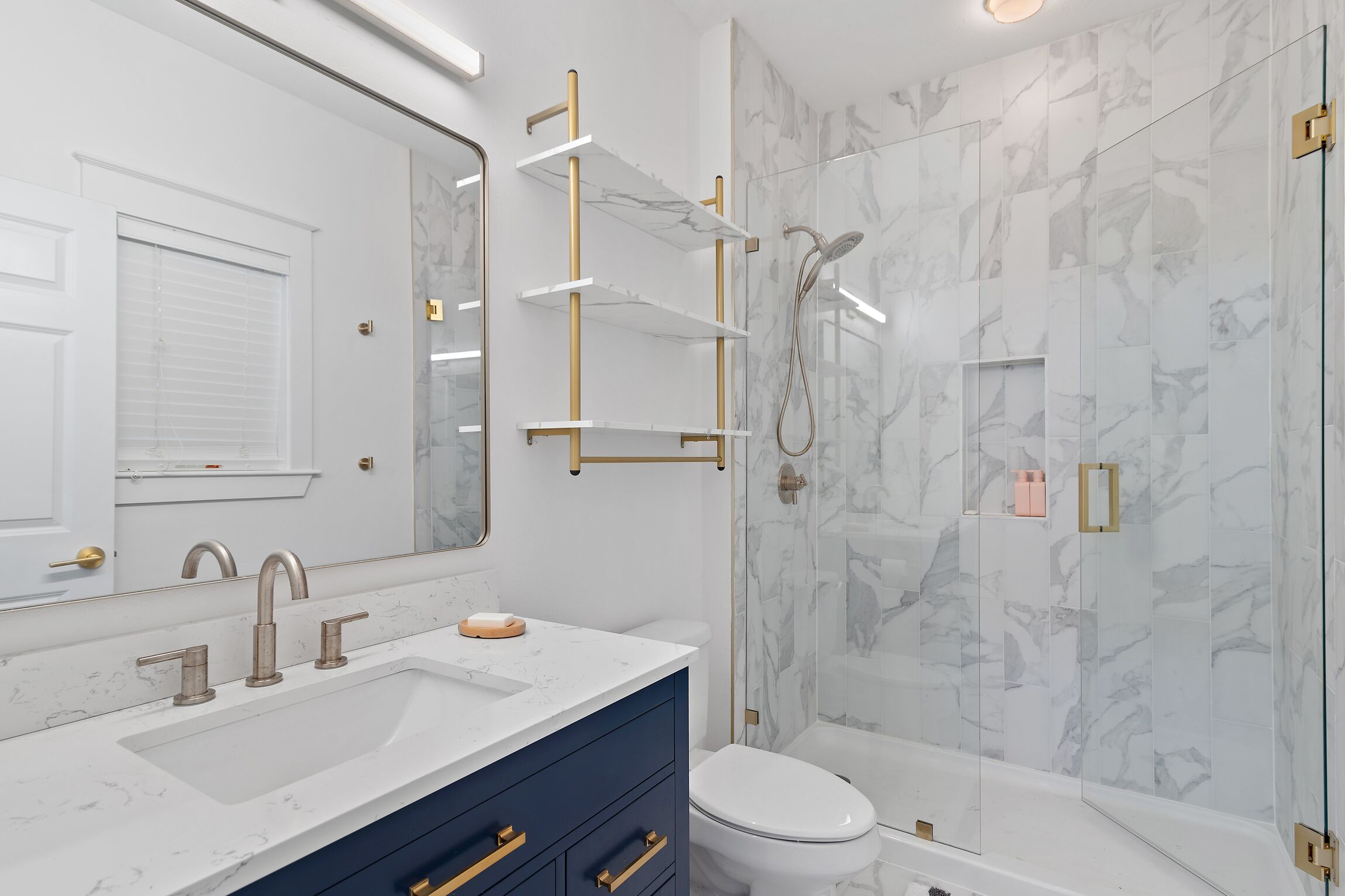 A modern bathroom with a marble sink, a glass-enclosed shower, and a white toilet.