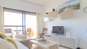 A modern living room with a sofa, a coffee table, a TV, and a balcony with chairs. - Magnificent 10th-Floor Studio with Sea Views (Marbella)