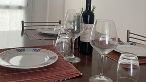 A dining table with plates, glasses, and a bottle of wine, set in a room with a window and an air conditioning unit. - Marina di Leuca Apartment (Marina di Leuca)