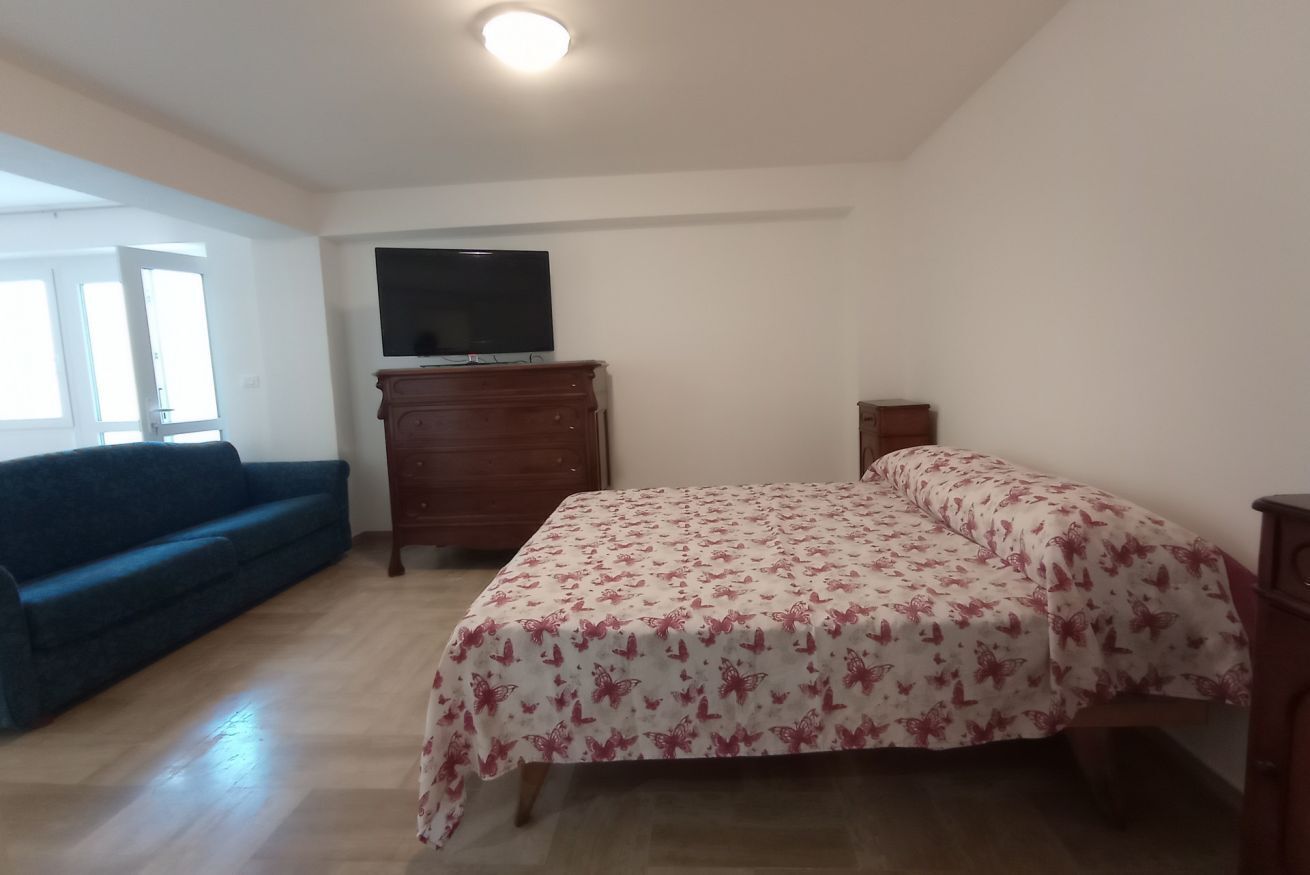 A bedroom with a bed, a dresser, a television on a stand, and a blue sofa.