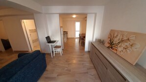 A modern living room with a blue sofa, a dining area with a table and chairs, and a kitchen in the background. - Marina di Leuca Apartment (Marina di Leuca)