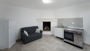 A compact kitchen with a built-in oven, a white refrigerator, and a dark-colored sofa. - Studio apartment Marina di Leuca (Marina di Leuca)