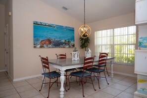 Uma área de refeições com mesa e cadeiras, um quadro na parede e uma janela com persianas.