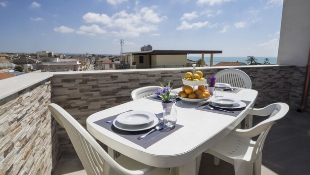 A table set for two with a view of the sea, stone walls, and a building in the background.