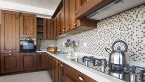 A modern kitchen with wooden cabinets, a tiled backsplash, and a stainless steel kettle on the counter.