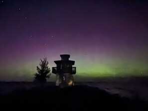 A lighthouse at night with a clear view of the sky and a green aurora. - Cozy Quiet Island Light House on Water Front (Fairgrove)