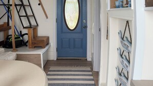 A blue door with a decorative glass panel, a wooden ladder, a sailboat decoration, and a nautical-themed wall display. - Cozy Quiet Island Light House on Water Front (Fairgrove)