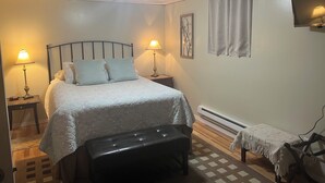 Ein Schlafzimmer mit einem Bett, zwei Nachttischlampen, einem Nachttisch, einer Bank, einem Heizkörper und einem an der Wand montierten Fernseher.