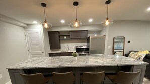 Une cuisine moderne dotée d’un grand îlot central, de tabourets de bar, de luminaires suspendus et d’appareils électroménagers en acier inoxydable.