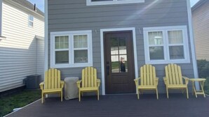 Une maison à deux étages avec un porche à l’avant, une porte marron et trois chaises Adirondack jaunes.