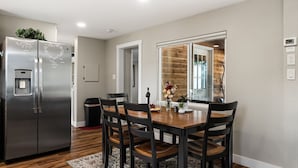 A modern kitchen with a stainless steel refrigerator, a dining table with chairs, and a wooden accent wall. - The Little House in the woods (Sagle)