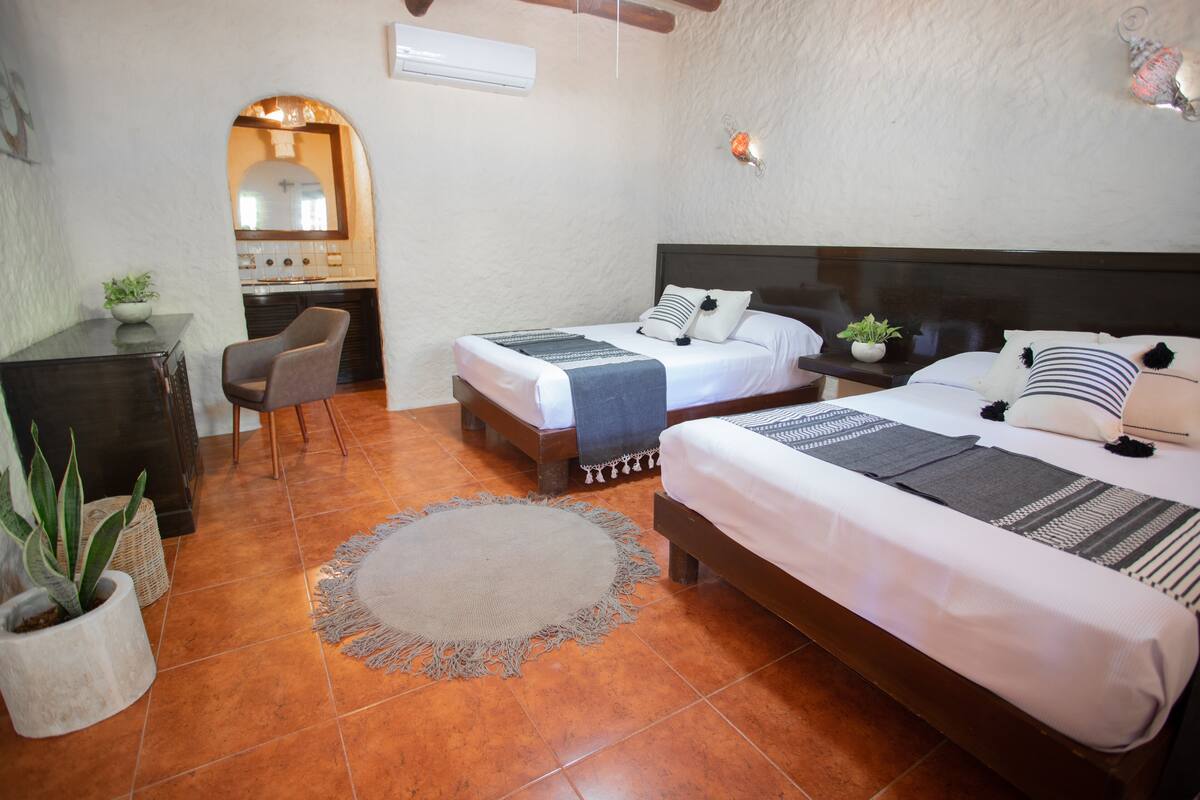Hotelkamer met twee bedden, een bureau en een stoel. Er ligt een rond tapijt op de vloer en staat een potplant op het bureau.