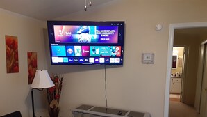 Una sala de estar con un televisor de pantalla plana montado en la pared, mostrando diferentes servicios de transmisión.