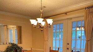 Una sala da pranzo con un tavolo in legno, quattro sedie, un lampadario, un grande specchio e vista all'esterno attraverso una porta vetrata.