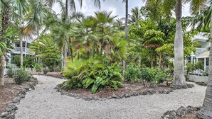 A tropical garden with palm trees and ferns, a gravel path, and a white fence. - Charming 'Boho Breeze' Retreat w/ Pool Access (Key West)
