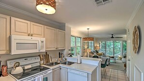 A modern kitchen with white cabinetry, a built-in microwave, and a dishwasher. There is a dining area with a table and chairs, and a large window providing natural light. - Charming 'Boho Breeze' Retreat w/ Pool Access (Key West)