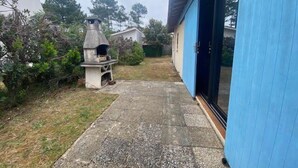 Un jardin avec un barbecue en pierre et une maison bleue.