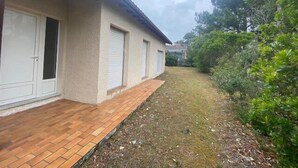 Un bâtiment avec un chemin de briques menant à une porte de garage, entouré de verdure et sous un ciel dégagé.
