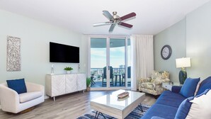 Ein modernes Wohnzimmer mit Flachbildfernseher, Deckenventilator, Sofa, Couchtisch und Blick auf die Stadt durch große Schiebeglastüren.
