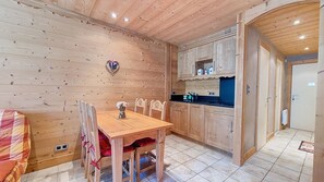 Interior de fusta amb taula de dinar, cadirees i zona de cuina amb armaris i un taulell.