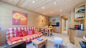 A cozy living room with a wooden sofa, a dining table, and chairs. There is a kitchen area with wooden cabinets and a countertop. - Apartment rental near the Rochebrune slopes (Megève)